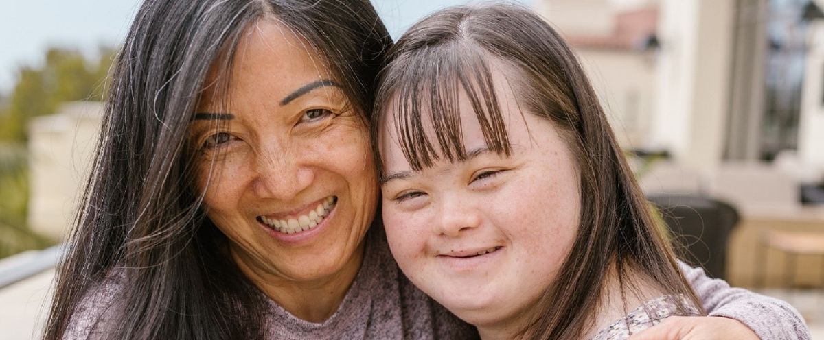 Down-Syndrom - Frau und Mädchen mit Down-Syndrom umarmen sich